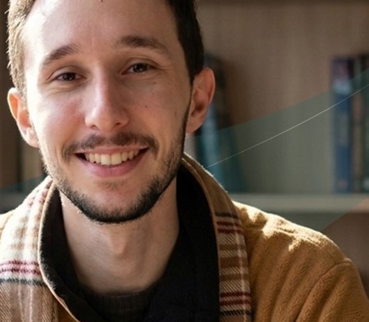 João Vitor, professor de História e orientador da Pouca Tese, sorrindo em uma biblioteca
